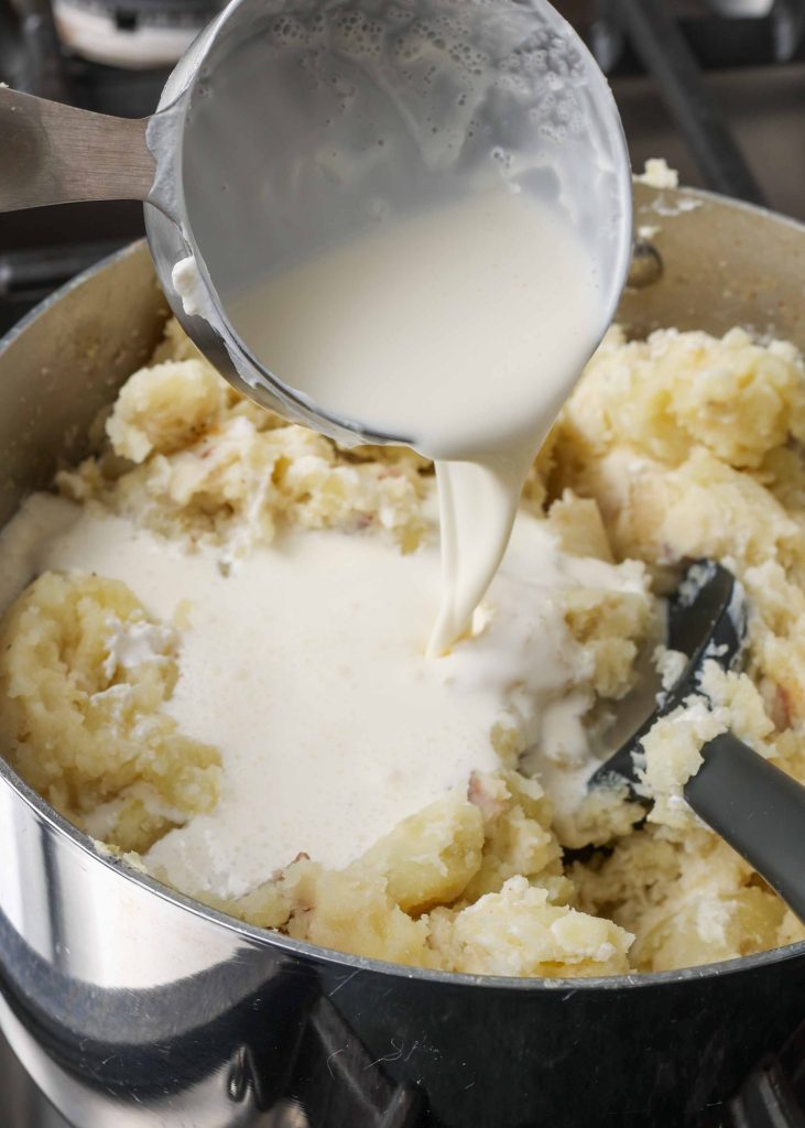 Overhead shot of mashed potatoes and cream cooking in a sauce pan with a rubber spoon