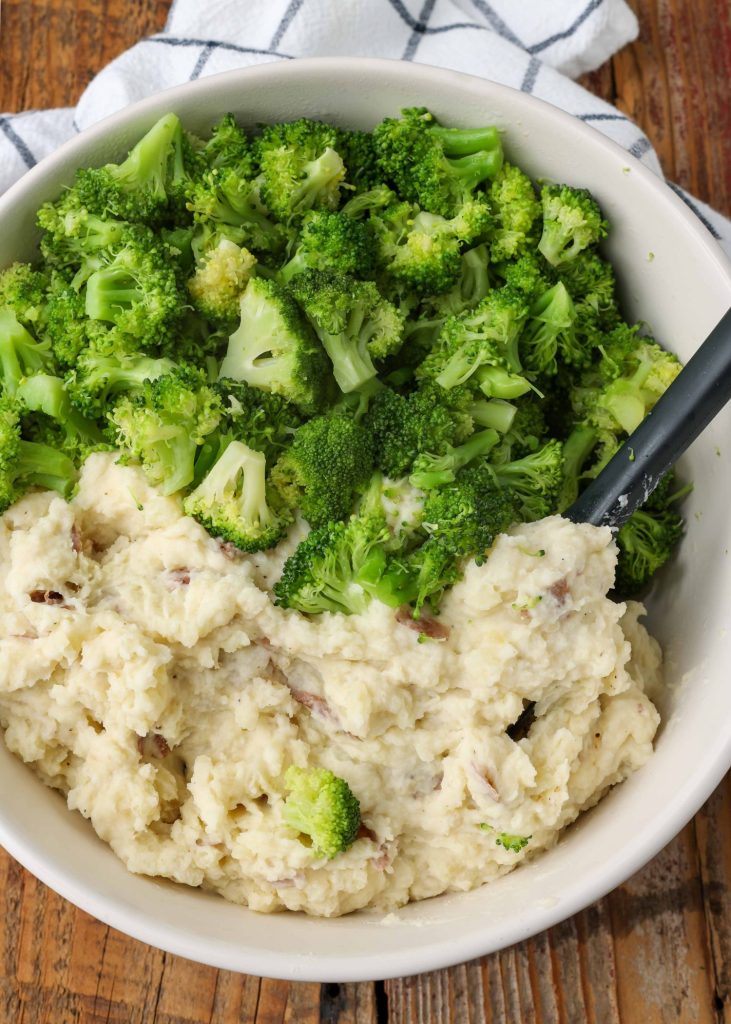 Overhead vertical shot of broccoli and mashed potatoes, served in a white bowl with a checkered white and black hand towel