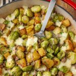 Vertical shot of brussels sprouts with sausage and potatoes, served in a red dish with a silver spoon