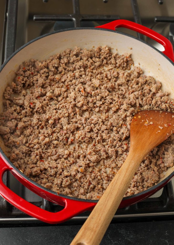 Overhead shot of ground beef cooking in a red dish with a wooden spoon