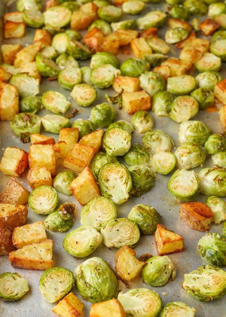 Brussels sprouts and sliced potatoes on a baking sheet