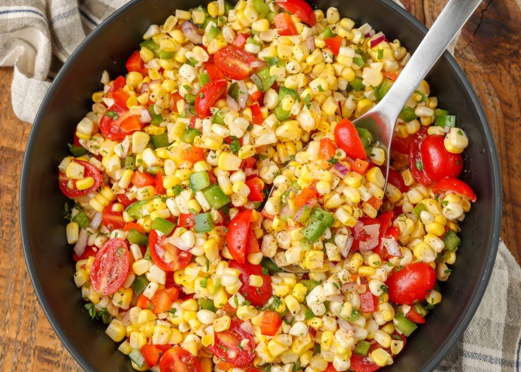 A horizontally aligned top down image of a serving bowl filled with colorful fresh corn salad.