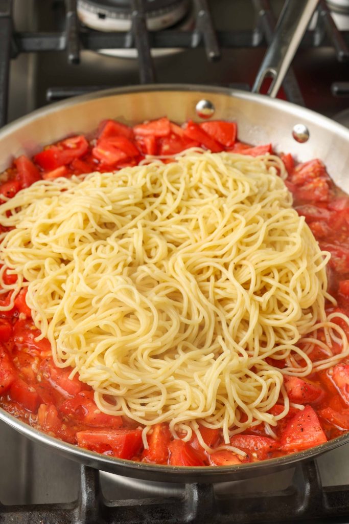 Cooked angel hair pasta has been piled atop the tomatoes in the pan.