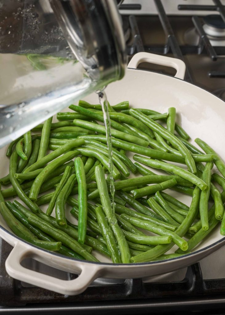 Vertical shot of green beans cooking in a white stove pan