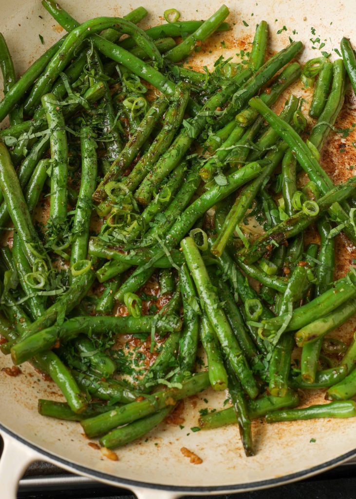Overhead shot of green beans with butter and herbs in a white stove pan