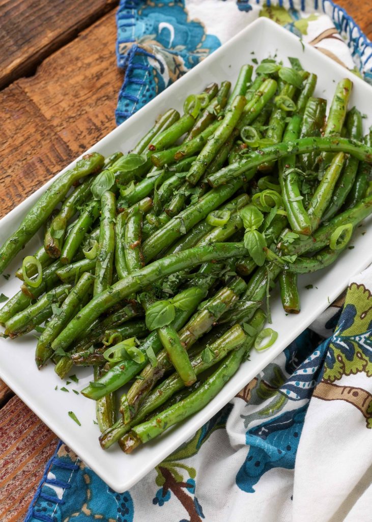 Vertical shot of green beans with butter and herbs, served in a long white platter with a blue floral print hand towel