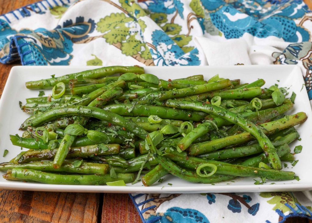 Horizontal shot of green beans with butter and herbs, served in a long white platter with a blue floral print hand towel