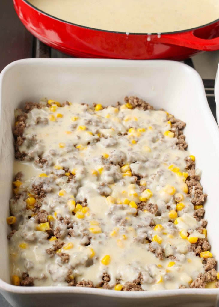 Overhead vertical shot of cheesy ground beef potato casserole in a long white tray mid-prep