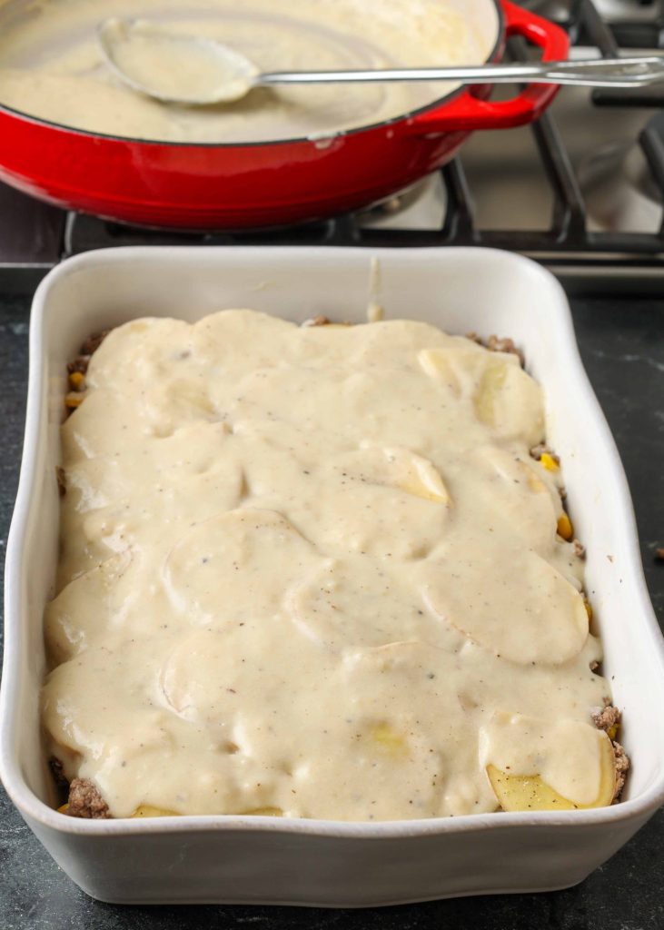 Vertical long shot of cheesy ground beef potato casserole in a long white tray just prior to cooking; the cheese has not yet been added