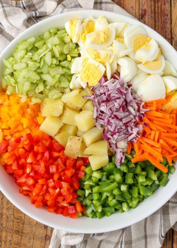 A vertically aligned, top down image of a bowl of artfully arranged, colorful vegetables to make a Loaded Vegetable Potato Salad.