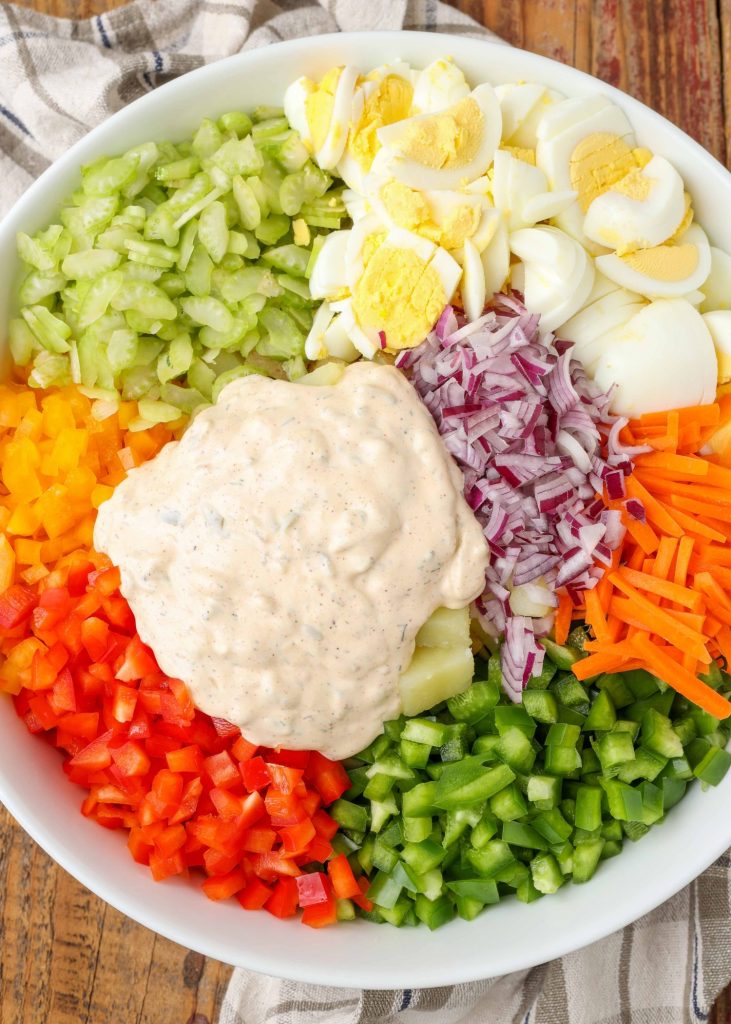 A top down image of a bowl of artfully arranged, colorful vegetables and the wet ingredients to make a Loaded Vegetable Potato Salad.