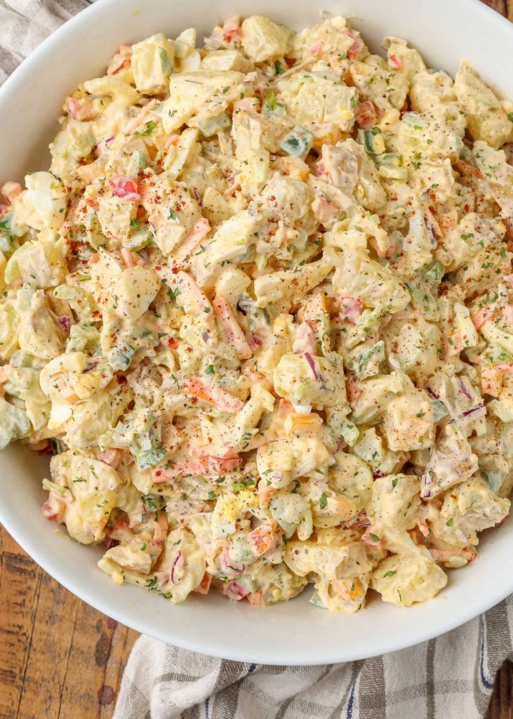 The potato salad ingredients have been mixed in the white bowl and are ready to serve.