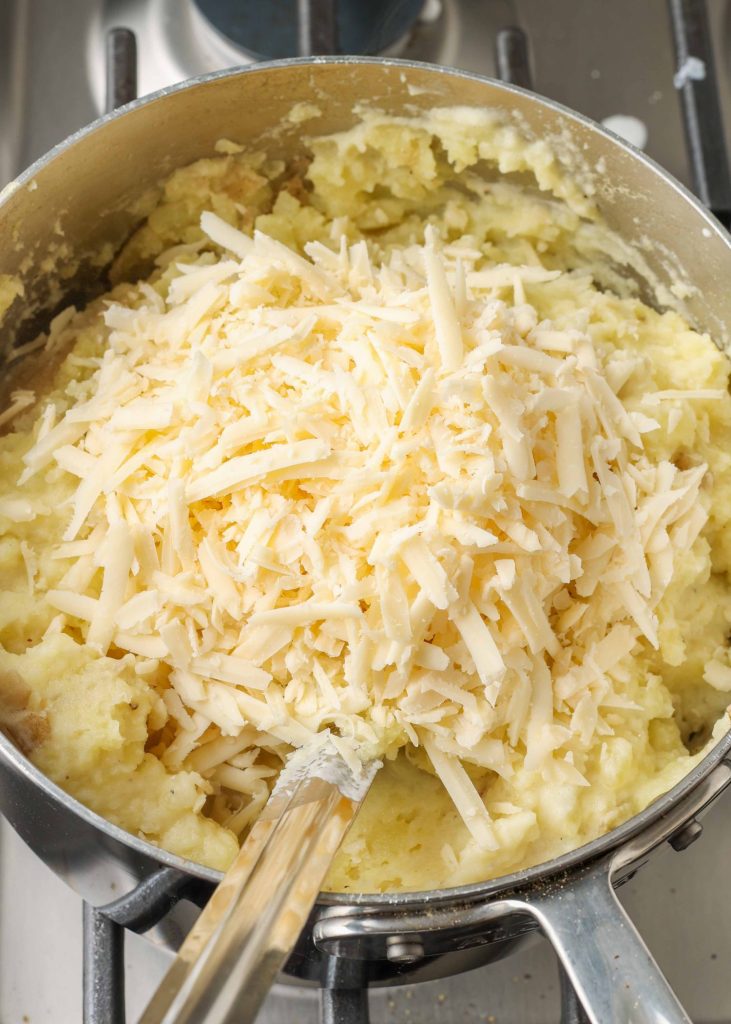 Creamy mashed potatoes topped with shredded cheese in a silver pot