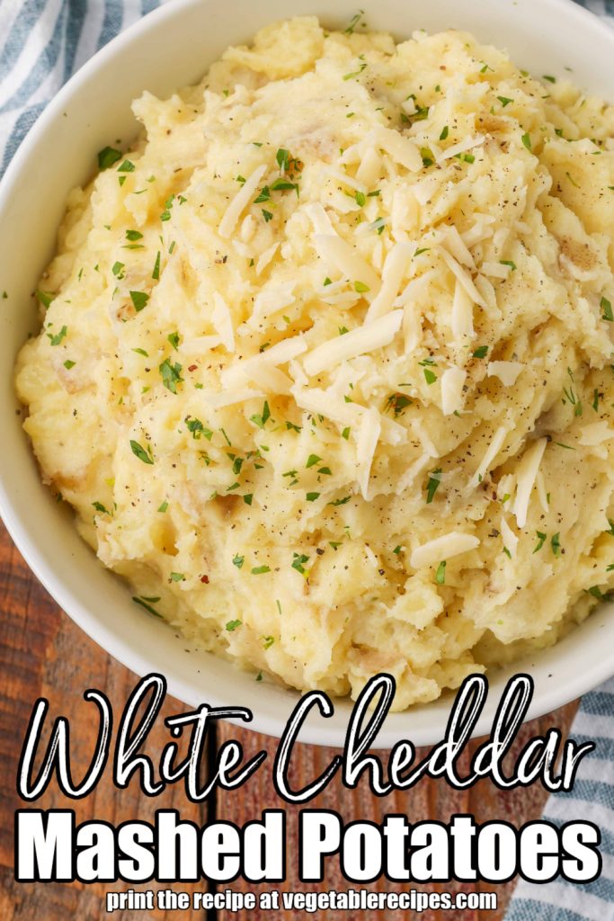 Overhead vertical shot of creamy white cheddar mashed potatoes topped with shredded cheese served in a white bowl; superimposed white text reads "White Cheddar Mashed Potatoes"