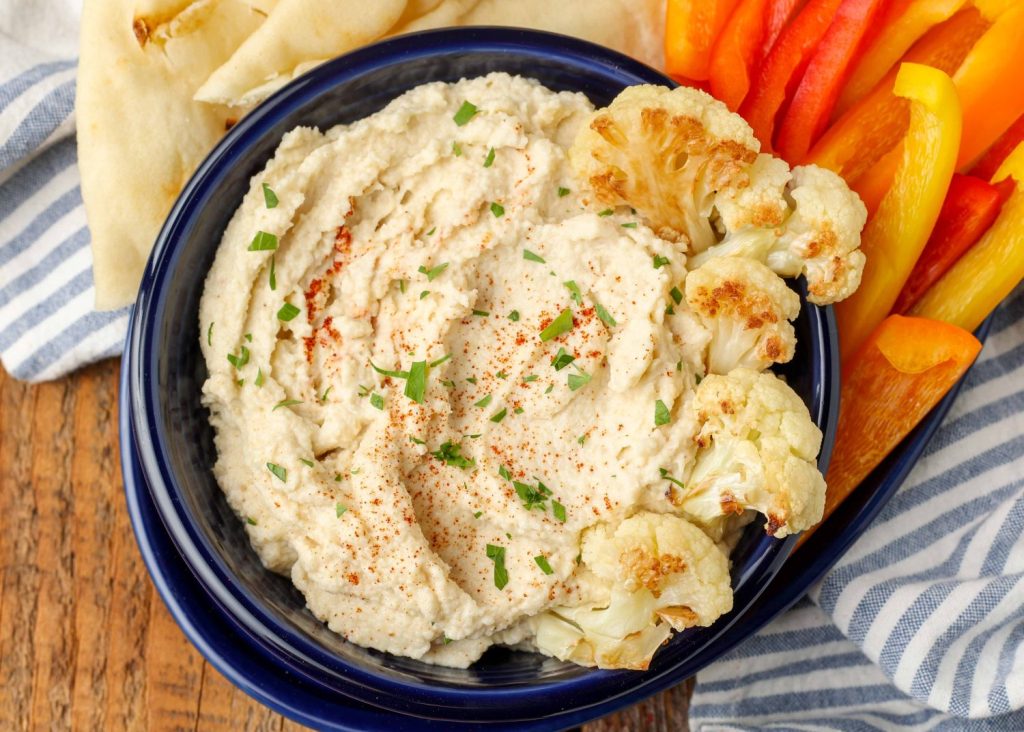 hummus in blue bowl surrounded by bell peppers and pita wedges