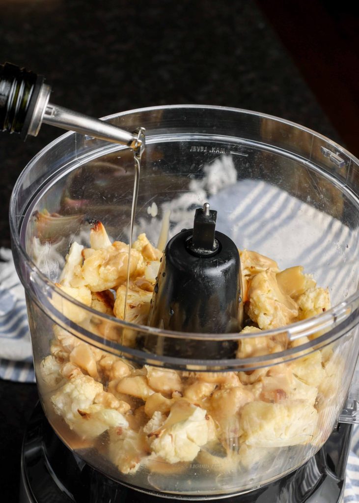 olive oil drizzled into food processor holding cauliflower