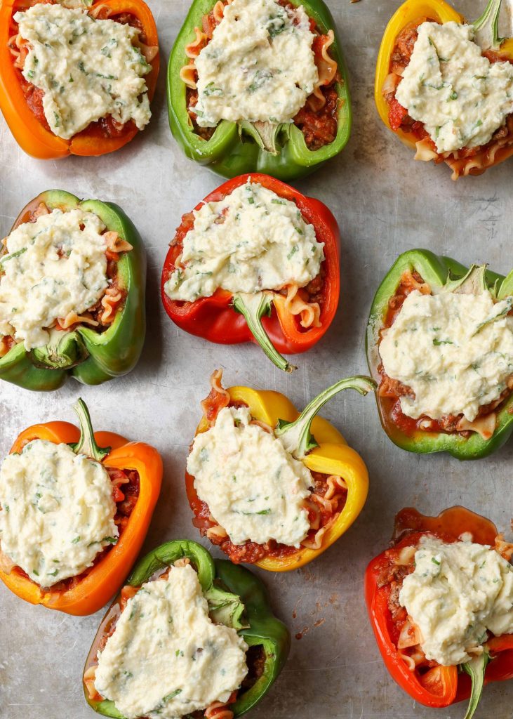 Colorful stuffed peppers with a cheesy topping are visible on a metal baking sheet in this top down photo.