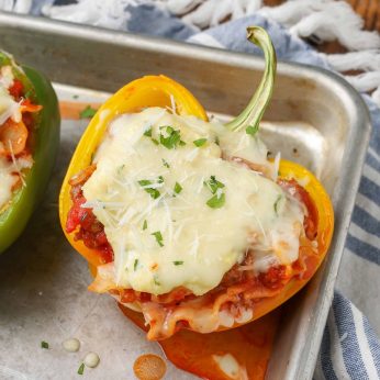 A stuffed pepper with a cheesy topping is visible on a metal baking sheet in this vertically aligned photo.