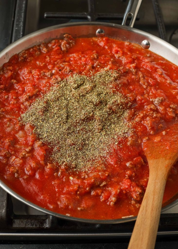 The seasonings have been added to the ground beef and tomato sauce in a metal pan.