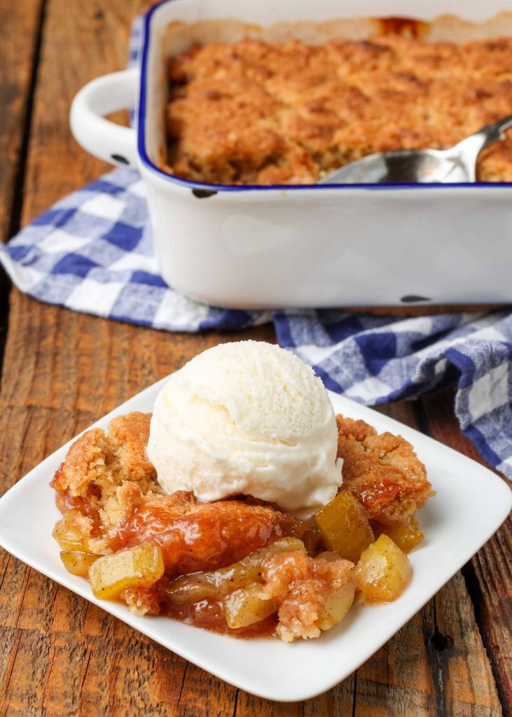 Zucchini Cobbler topped with ice cream on white plate next to blue and white checked napkin