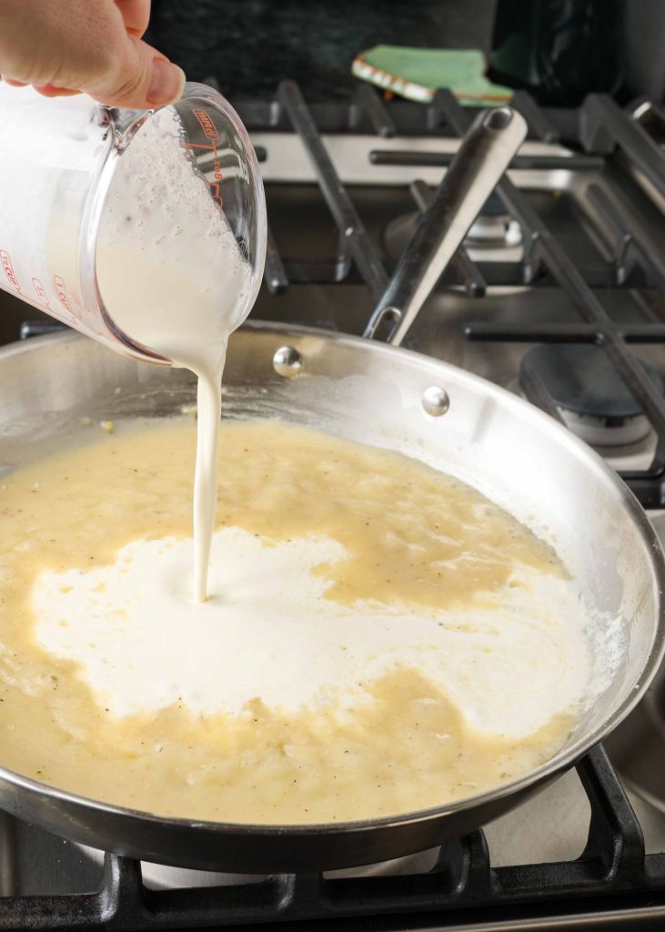 cream being poured into sauce in pan
