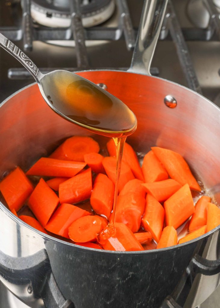 Pouring honey onto carrots in pan