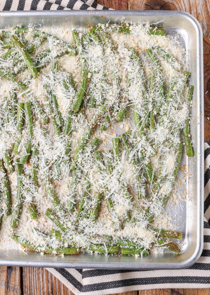 Green beans topped with grated parmesan cheese on a baking sheet