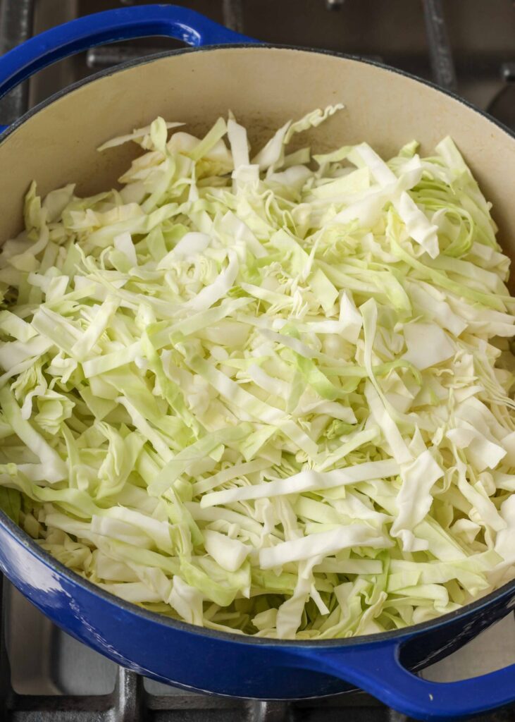 Fresh cabbage has been sliced and placed in the pot with blue handles.