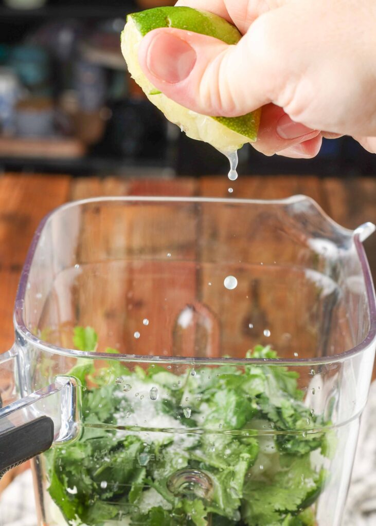an action shot of squeezing lime juice over the ingredients in the blender.