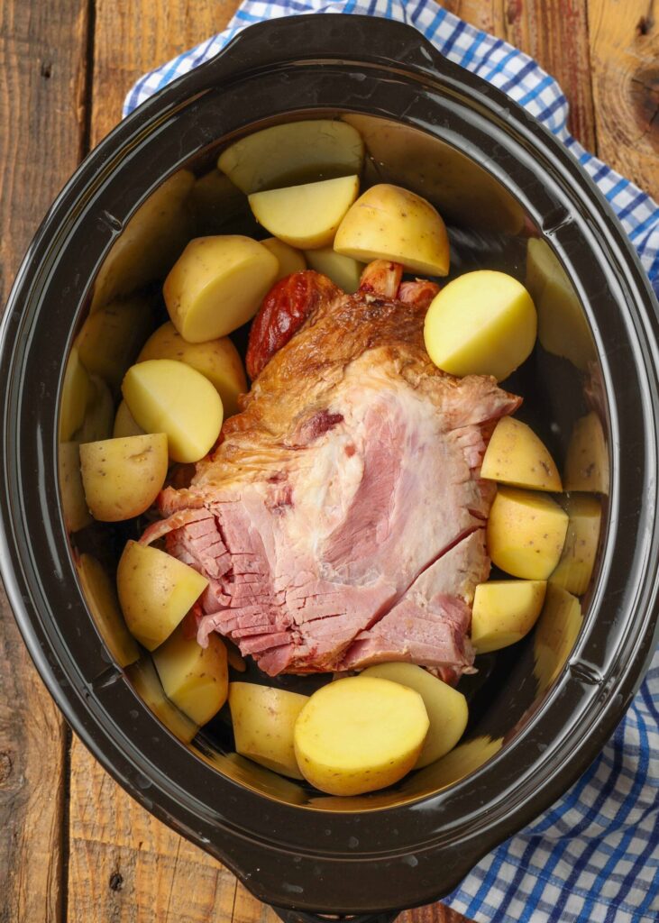 The ham shank is in the crock pot and there are chunks of potatoes that have been placed around the edges.