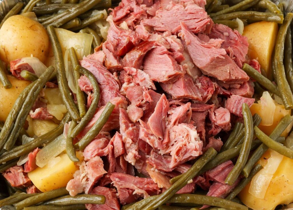 A horizontal close up photo of chunks of ham, green beans and yellow potatoes.