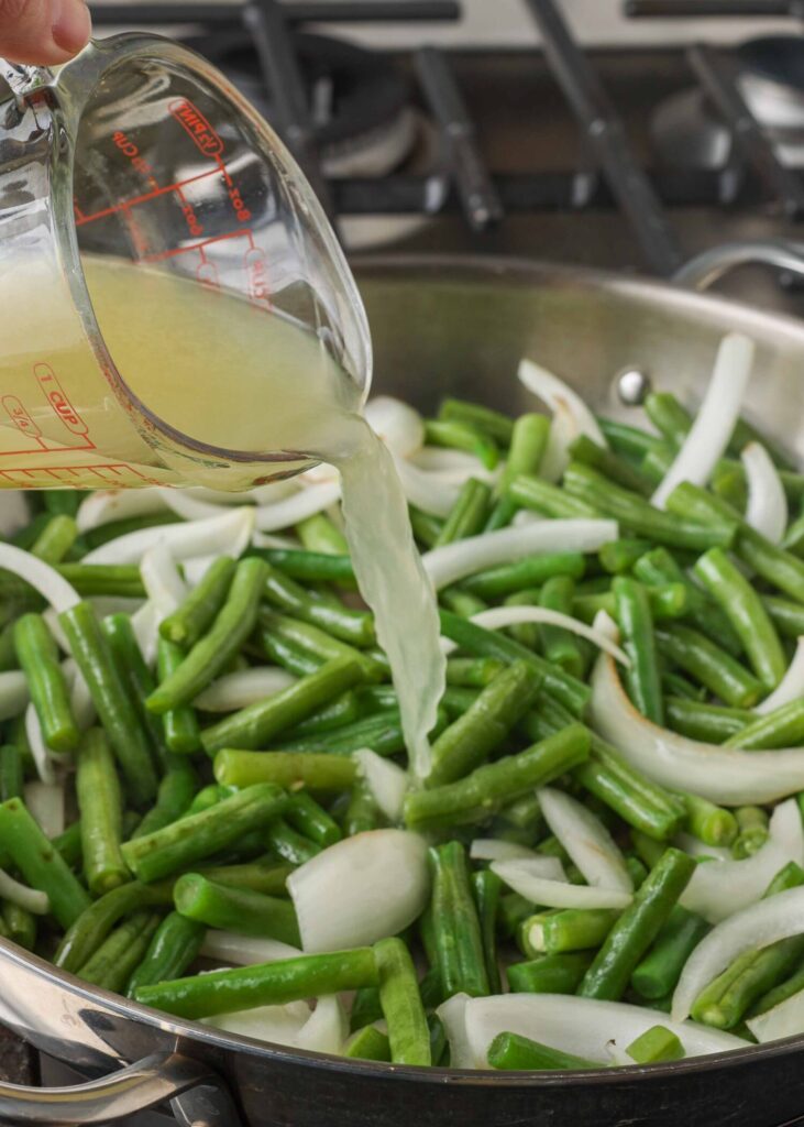A pour shot over the green beans and onions in the pan.