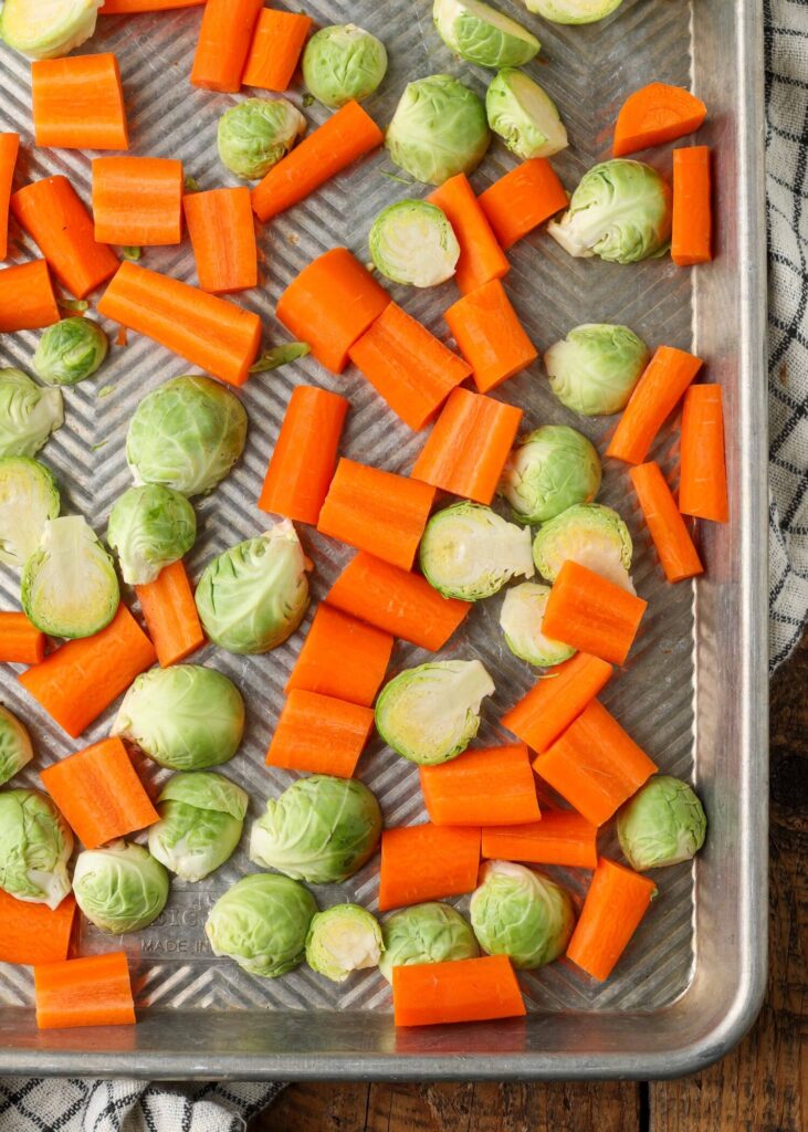 carrots and brussels sprouts have been spread out on a metal baking sheet in this vertical image.
