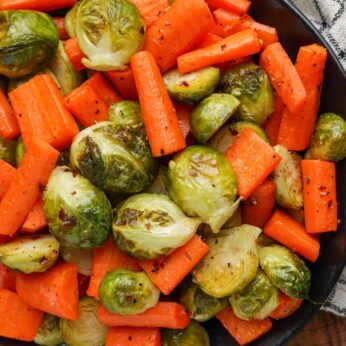 roasted brussels sprouts and carrots in a dark bowl over a checkered tea towel.