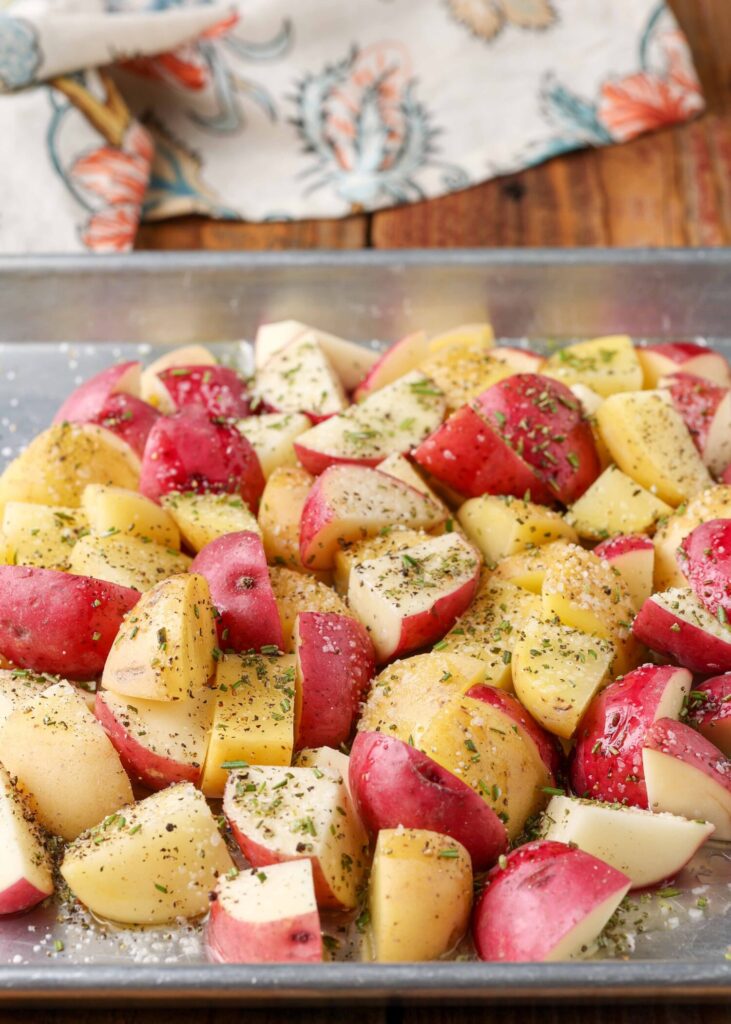 The red potatoes have been tossed in oil and seasoned on a pan.