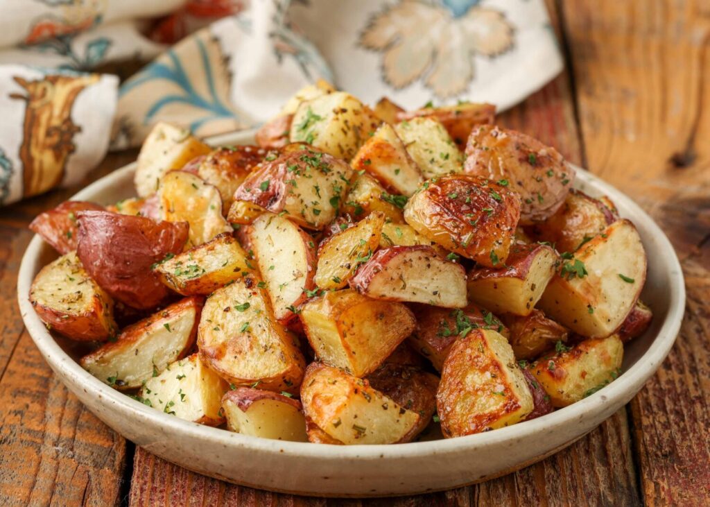 A horizontally aligned image of a round white plate piled high with seasoned red potatoes.