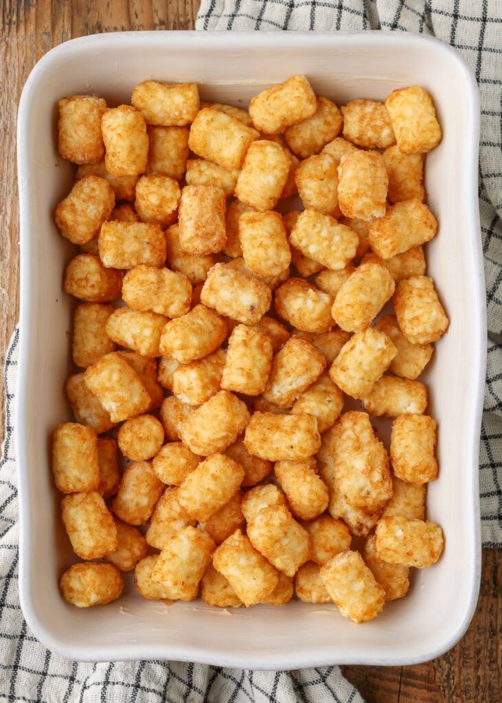 tater tots have been layered across the bottom of a white ceramic baking dish in this top down photo.