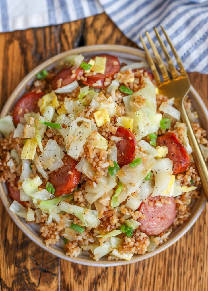 cabbage fried rice with sausage on pottery plate with gold fork