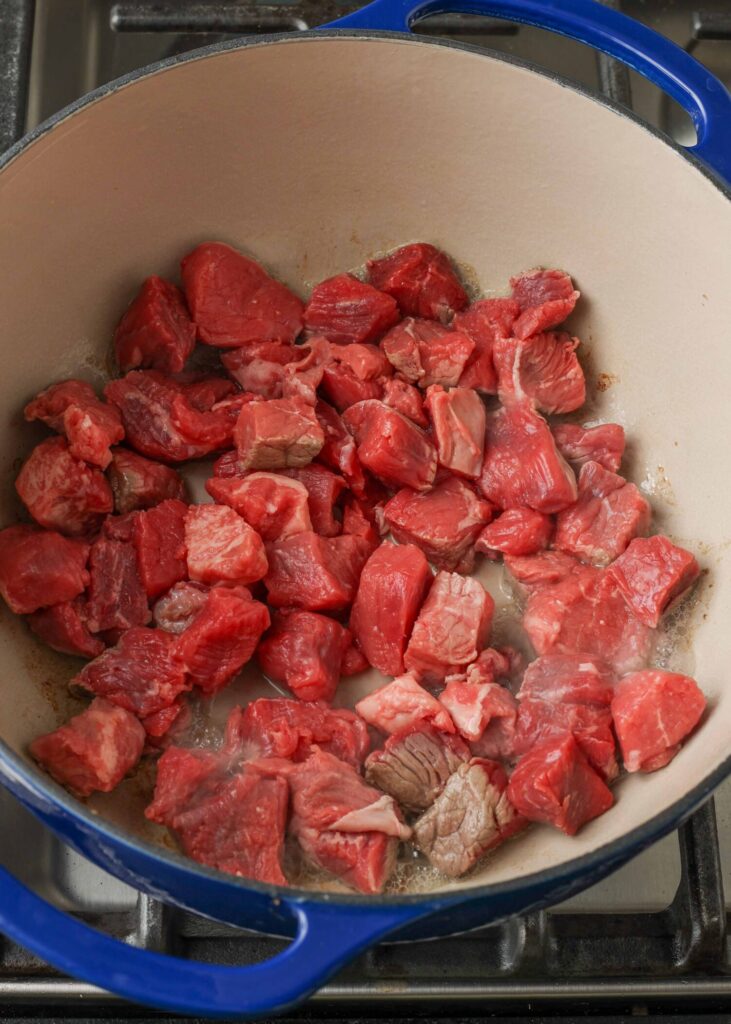 Steak sliced into 1/2-inch cubes cooking in blue pot
