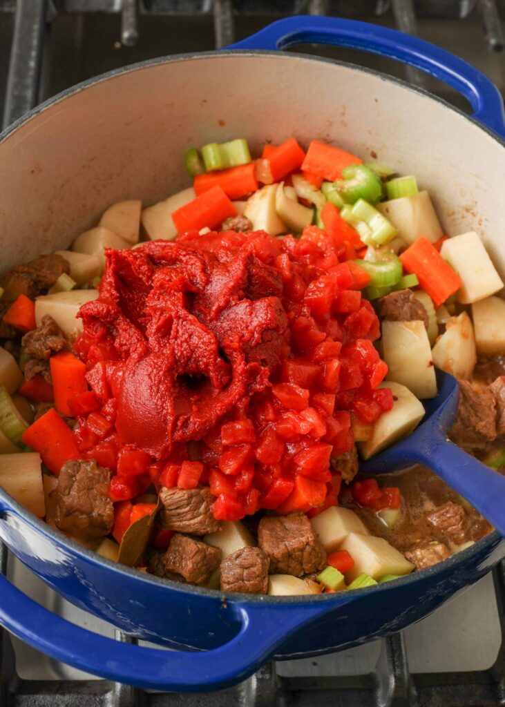 Steak, potatoes, celery, carrots, diced tomatoes, and tomato paste in blue pot