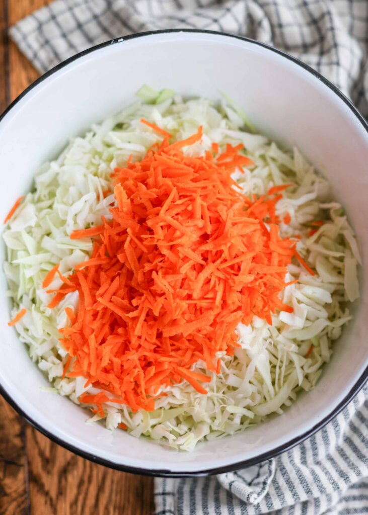 shredded carrot has been piled atop the chopped cabbage in a large white bowl.