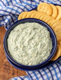spinach artichoke dip in blue bowl surrounded by crackers