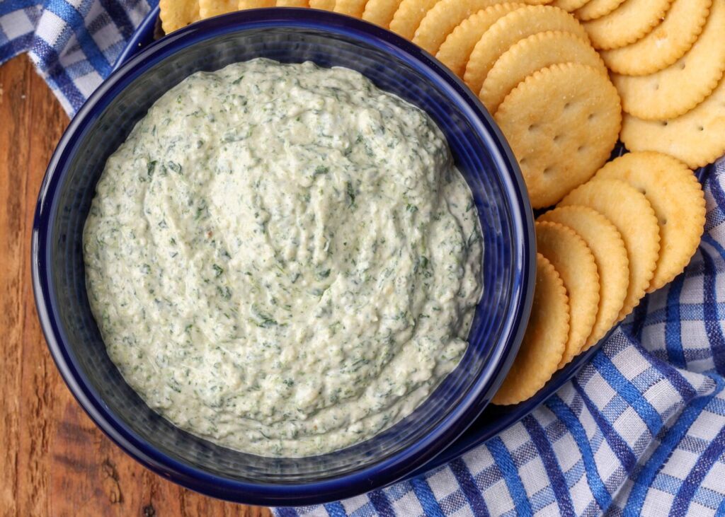 spinach dip in dark blue bowl with crackers