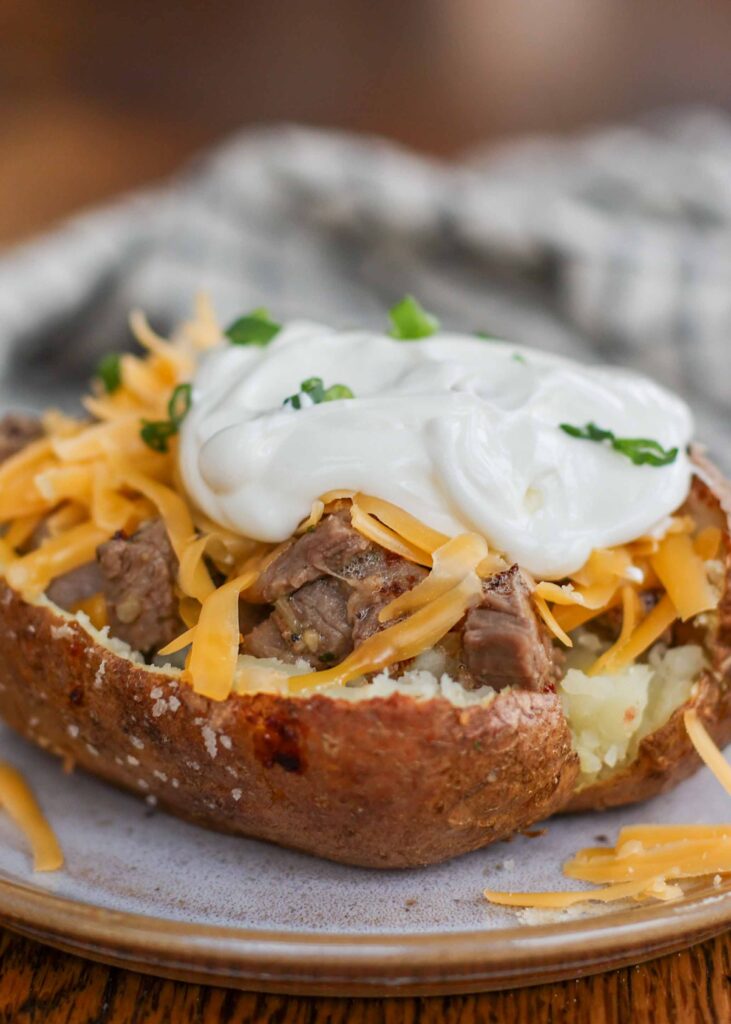 a generous dollop of sour cream has been placed on top of the steak baked potato with shredded cheese.