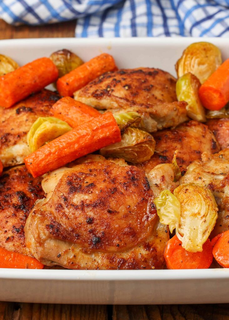 close up photo of roast chicken with vegetables in white pan with blue napkin