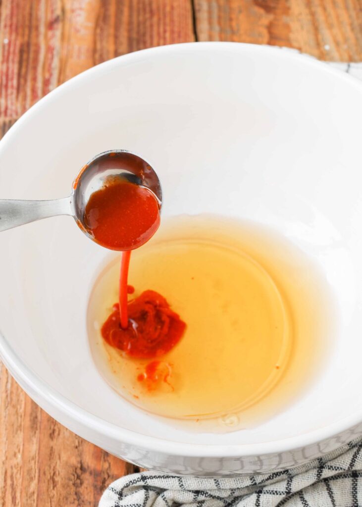 oil, vinegar, and hot sauce being measured into bowl