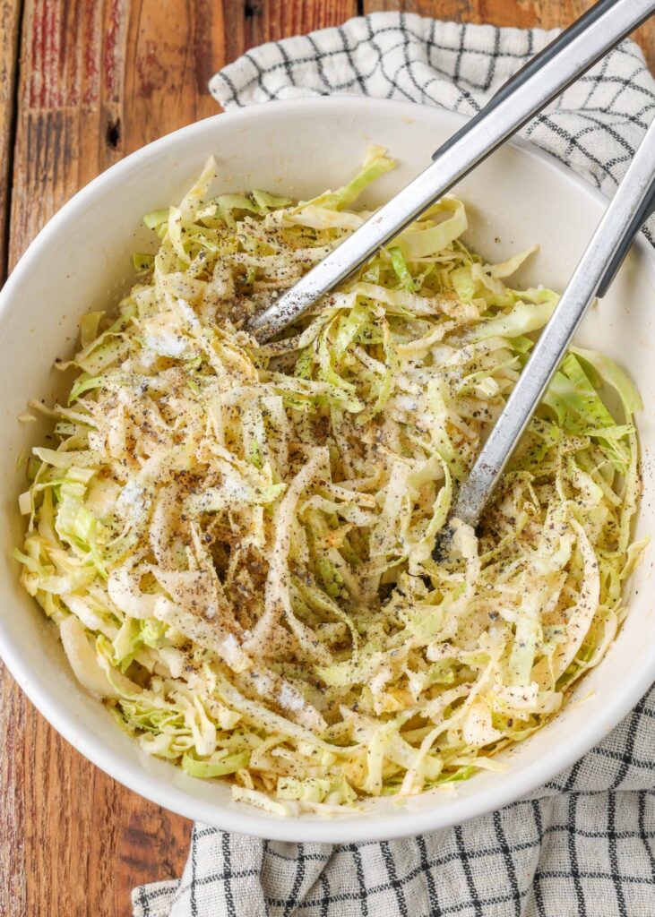 seasoned cabbage in large bowl with tongs