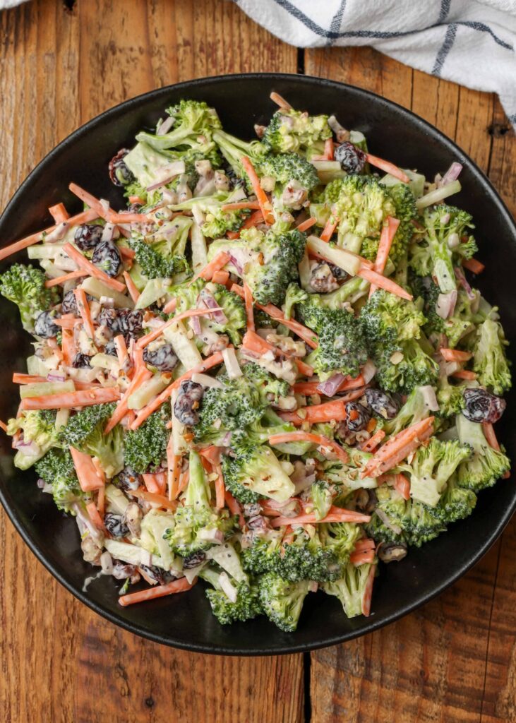 Broccoli slaw with carrots, red onion, cranberries, and pecans in a black bowl on a wooden table