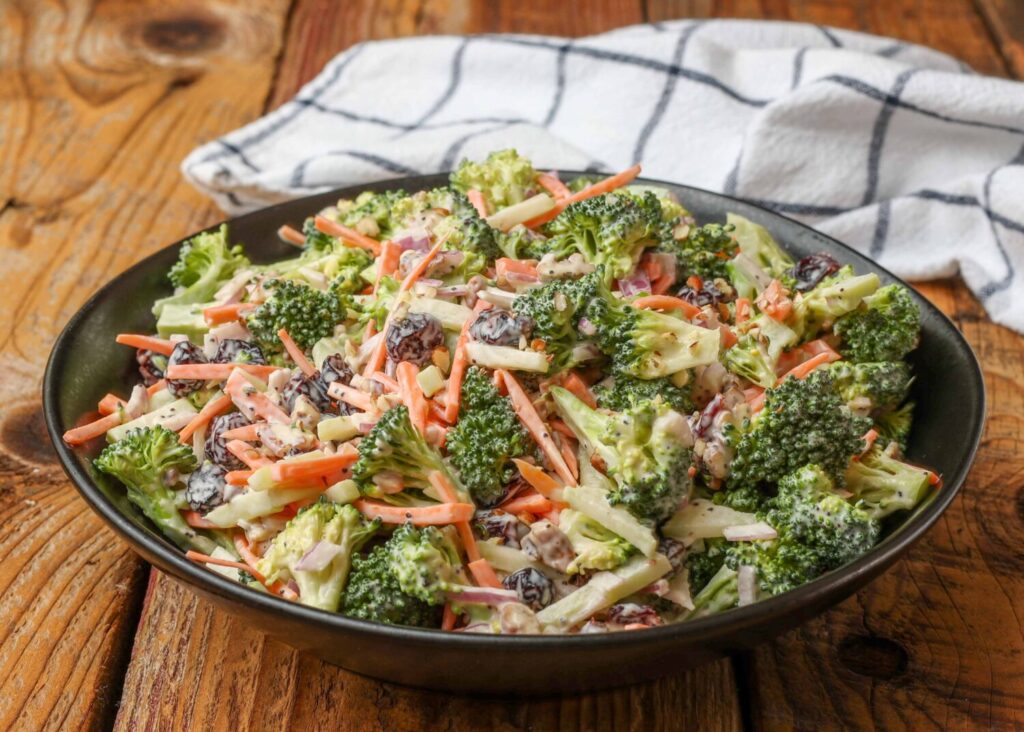 Broccoli salad with carrots, red onion, cranberries, and pecans in a black bowl on a wooden table
