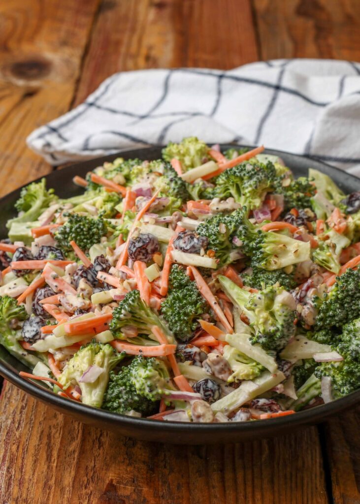 black bowl on wooden table holding a salad with broccoli, carrots, onion, and cranberries